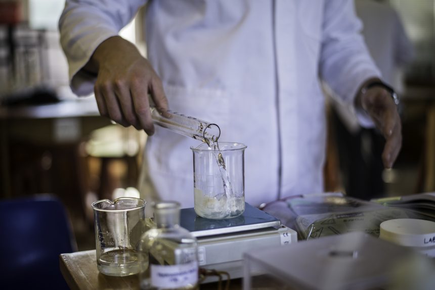 An A Level Chemistry student pouring a solution into a conical flask.