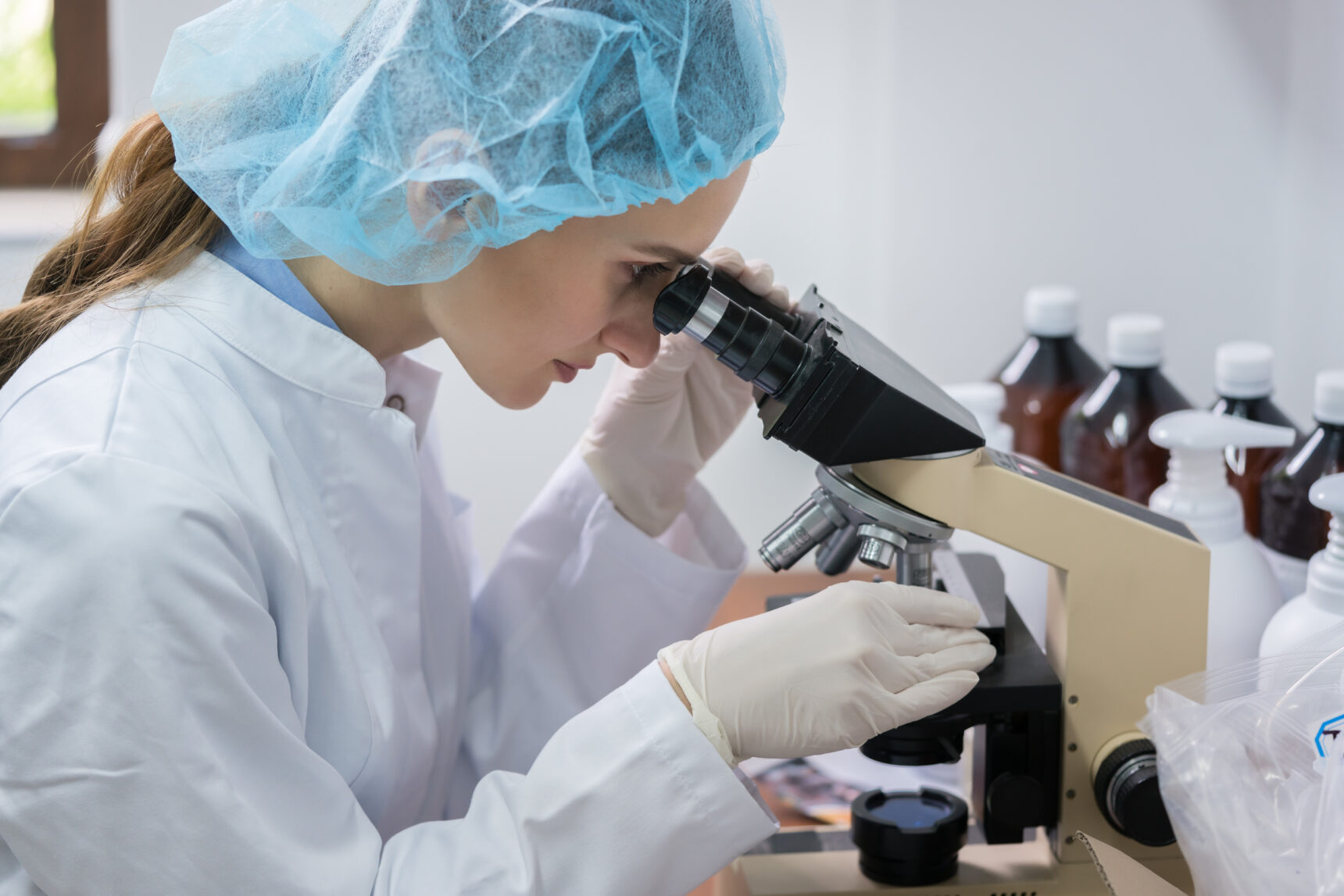 A female scientist wearing safety equipment whilst using a microscope in the laboratory.