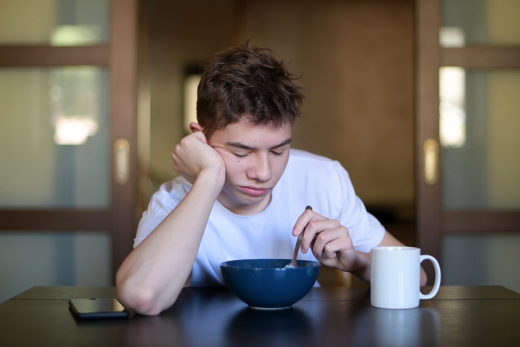 Tired teenage boy eating breakfast.