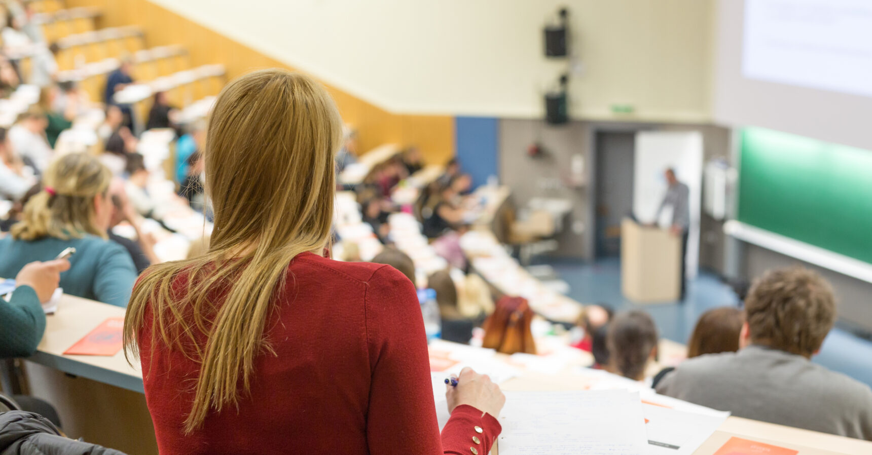 Blonde girl sat in a lecture theatre at university.