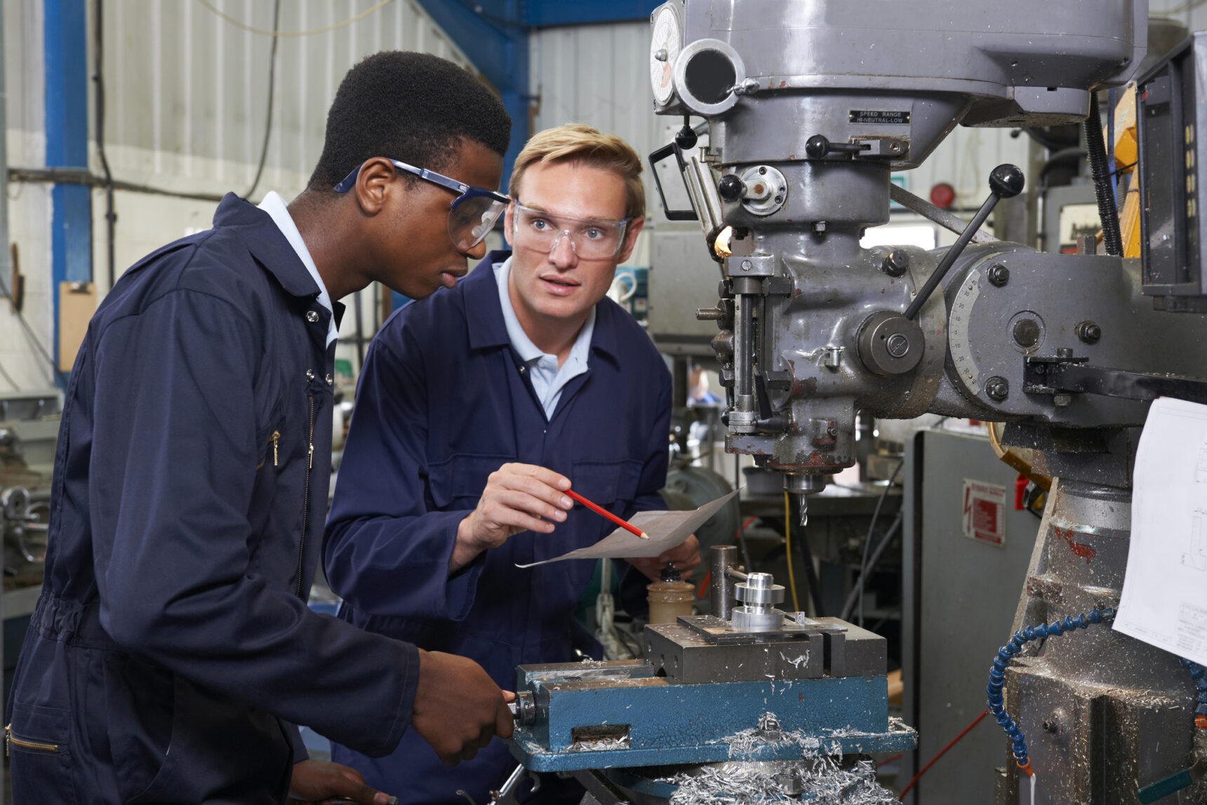 Engineer showing male apprentice how to use piece of factor equipment.