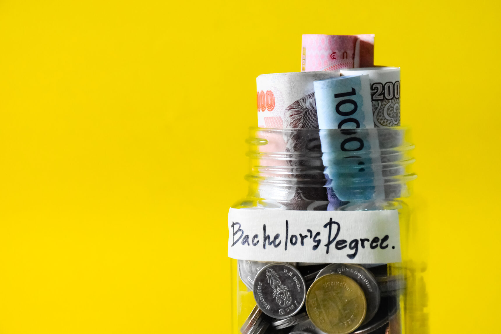 Cash savings in a glass jar with bachelor’s degree label stuck on the front.