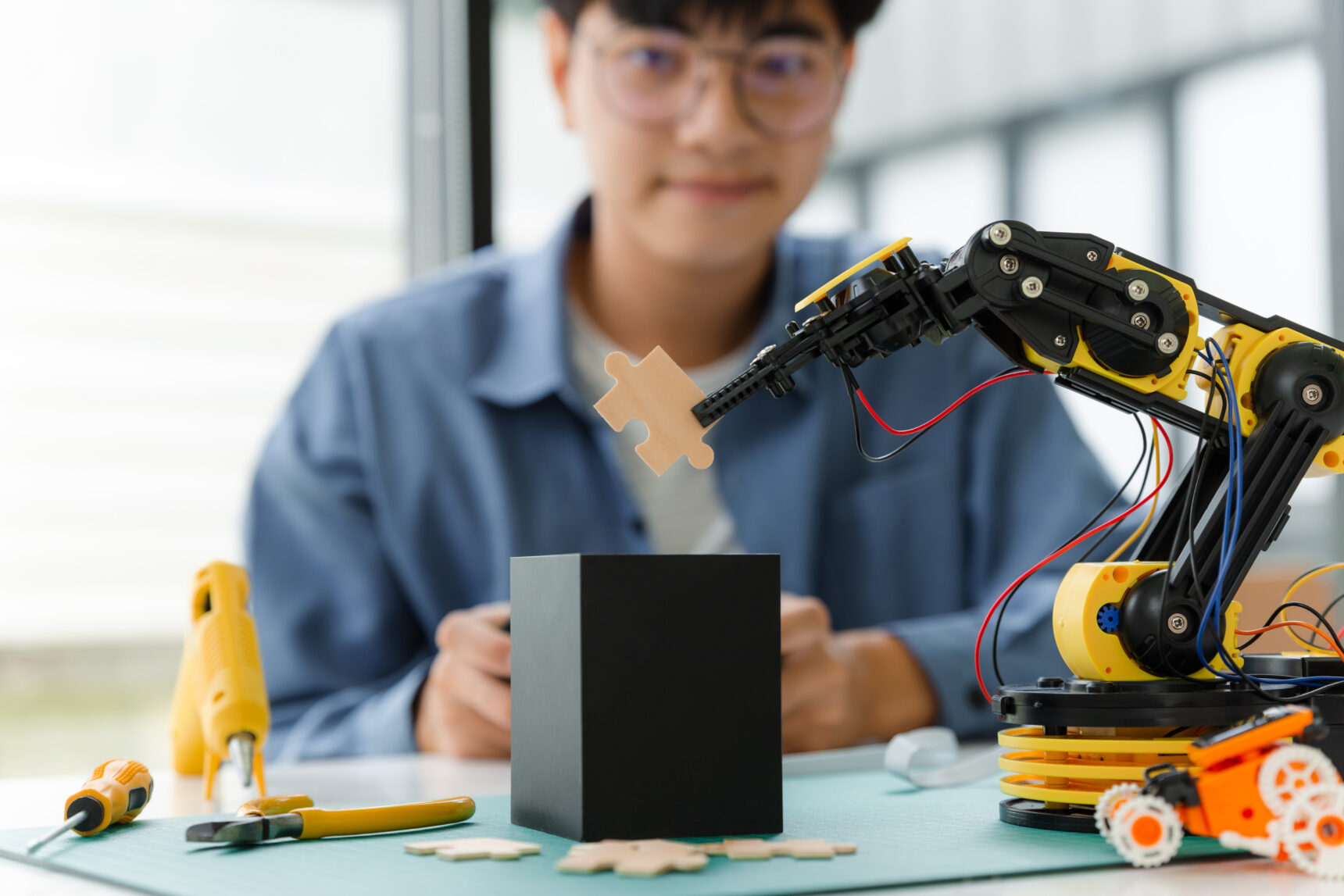 Student in glasses moving jigsaw piece using robot.