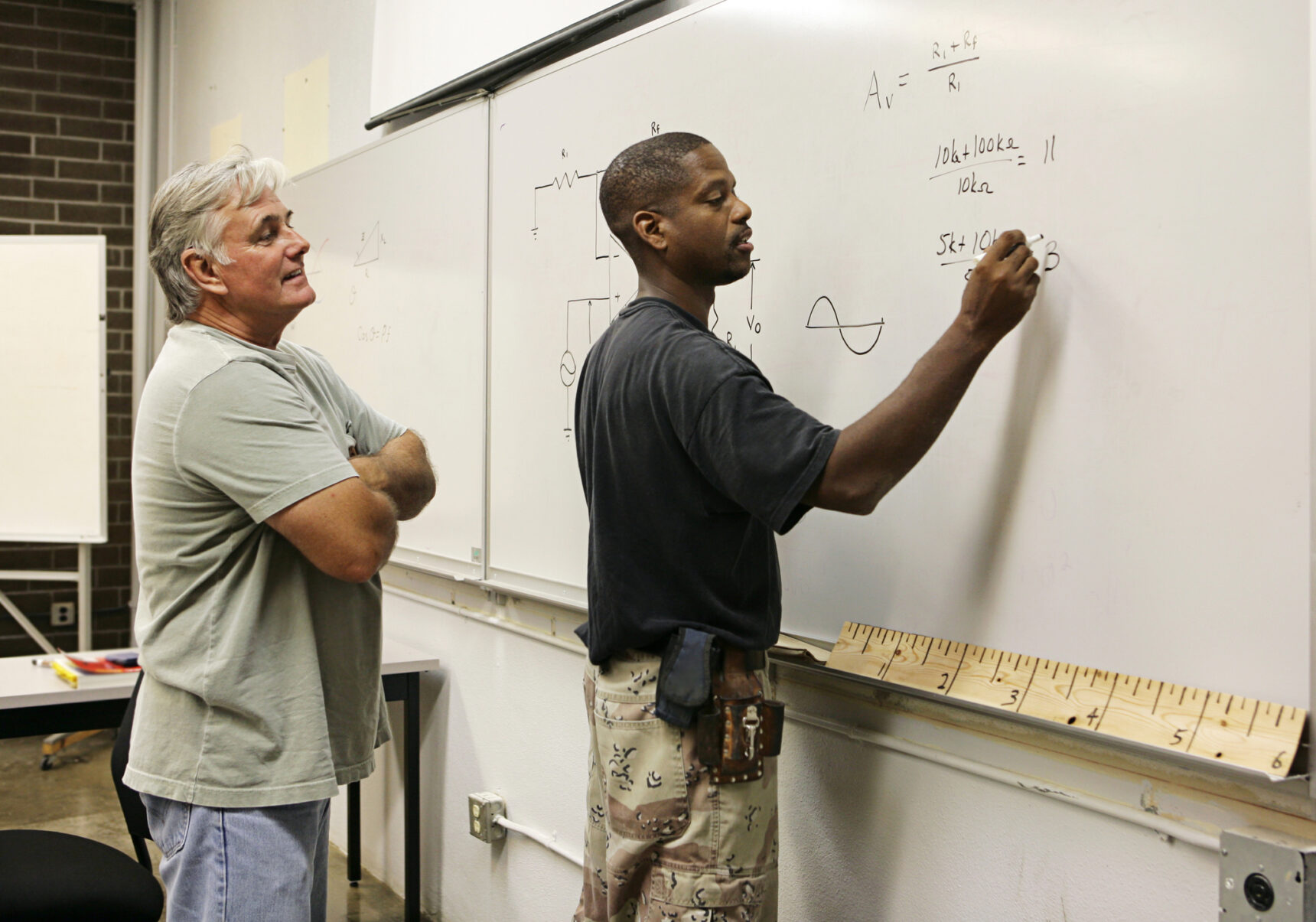 A T Level teacher looking on as a student solves equations on the whiteboard.