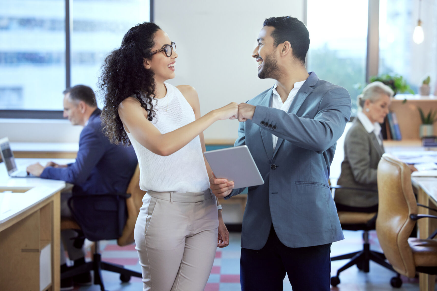 Smiling man and woman fist bump in business attire