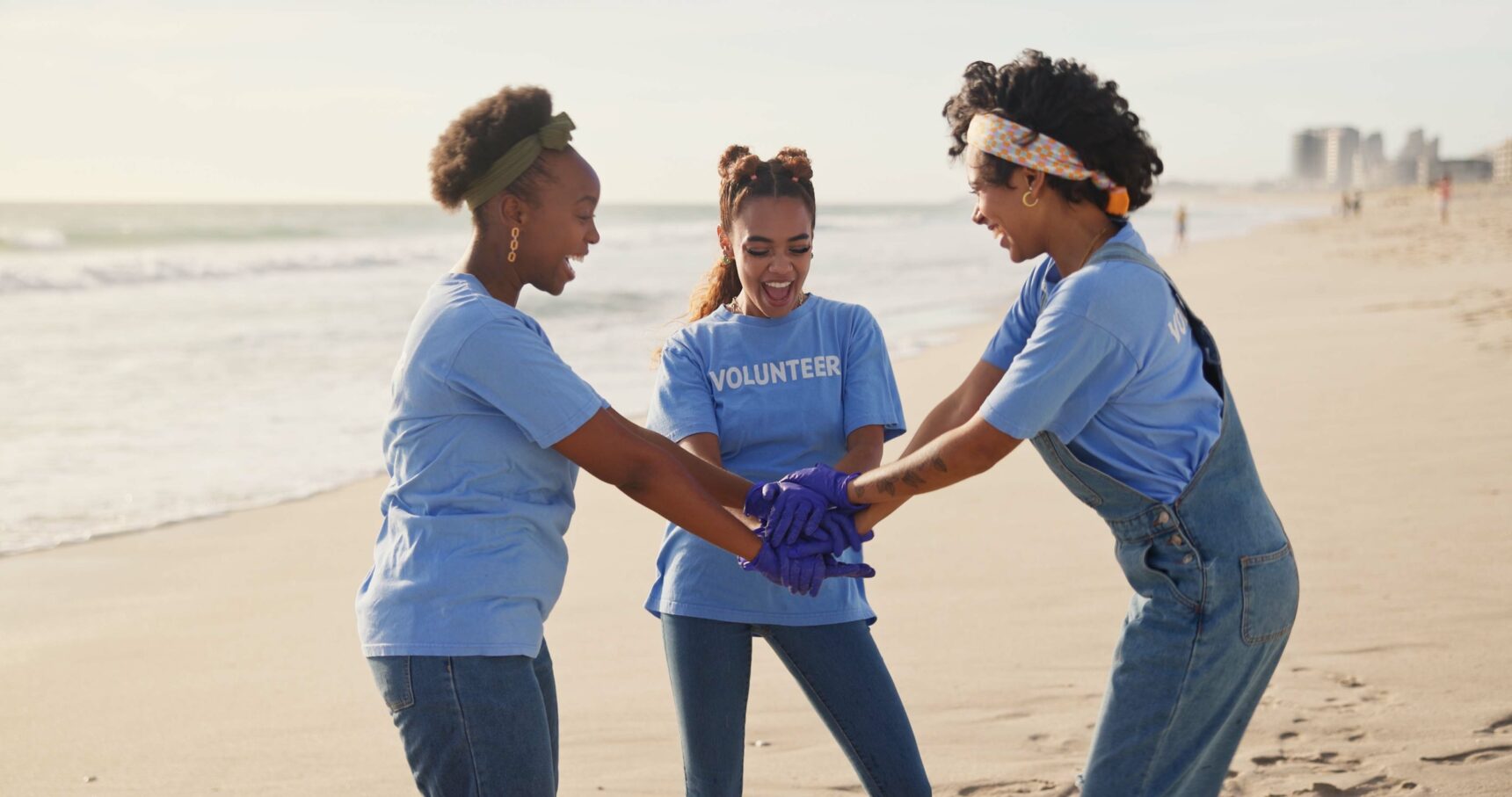 Three women on a gap year doing handshake on the beach and wearing volunteer t-shirts.