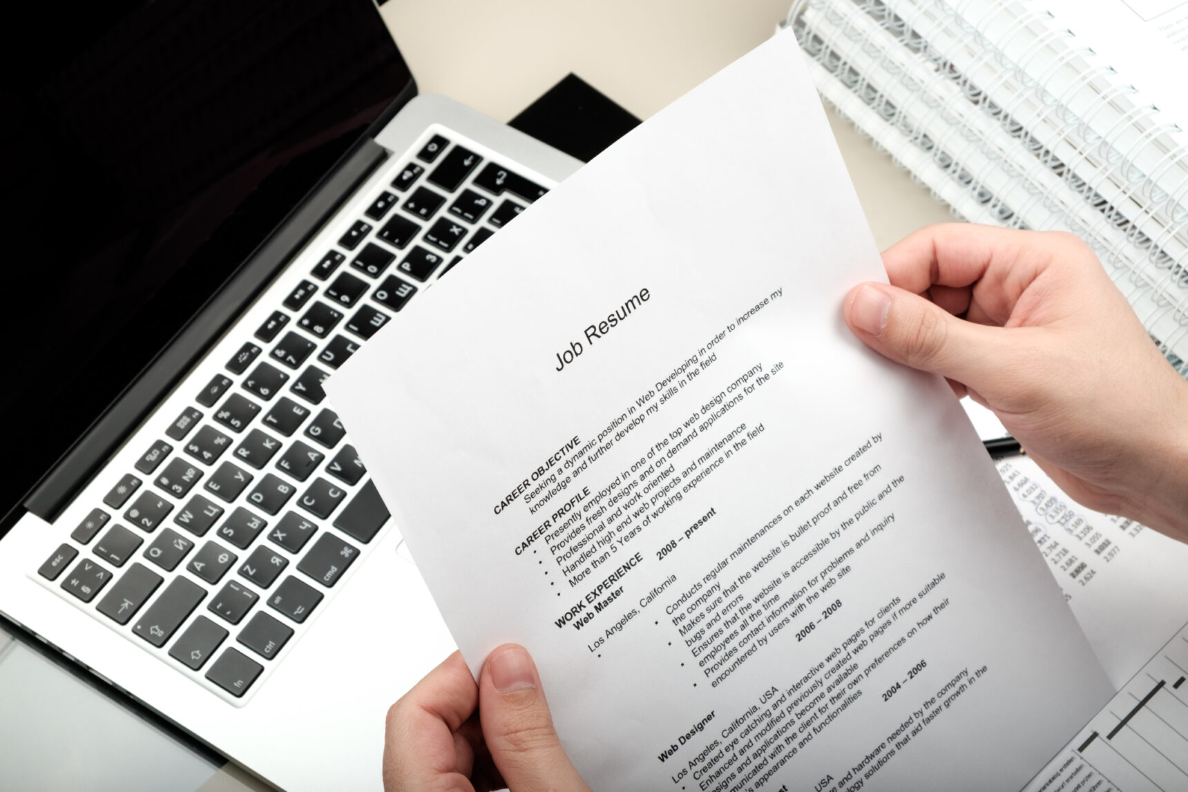 Someone holding their printed CV with a laptop in the background.