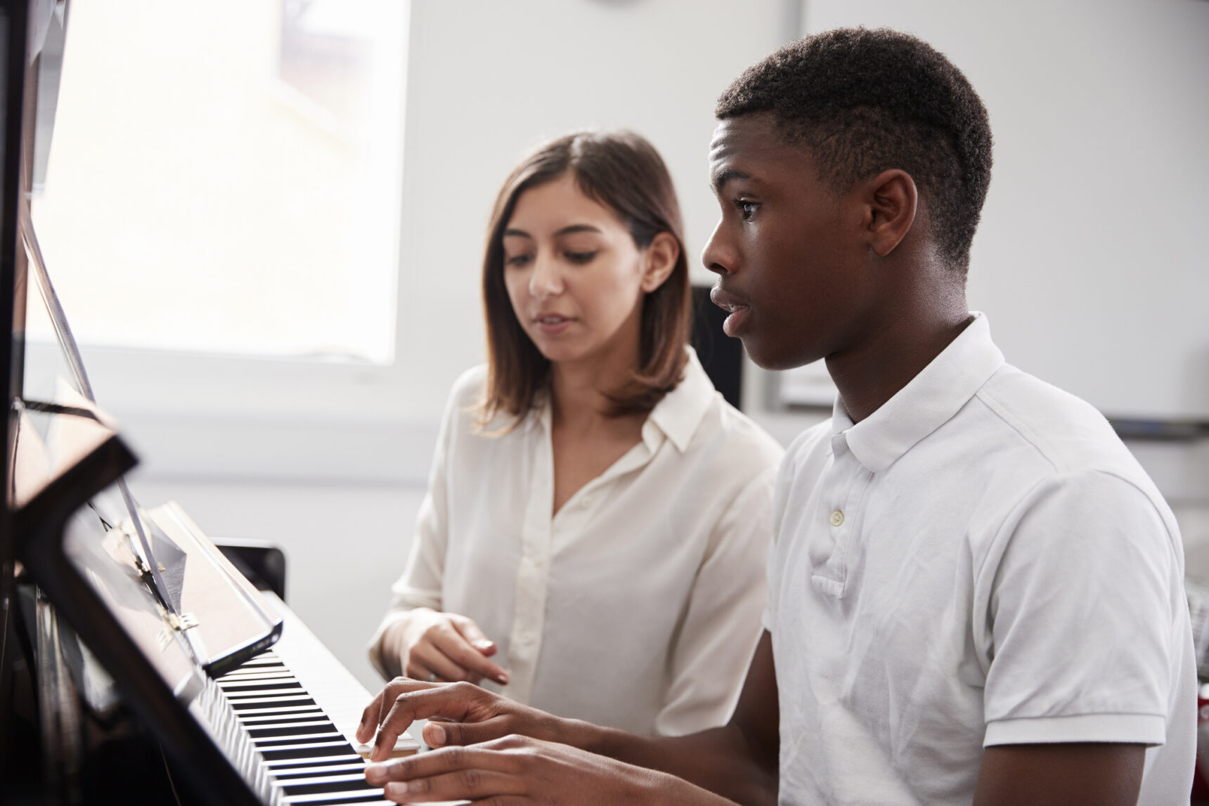 Male pupil with teacher playing piano in music lesson