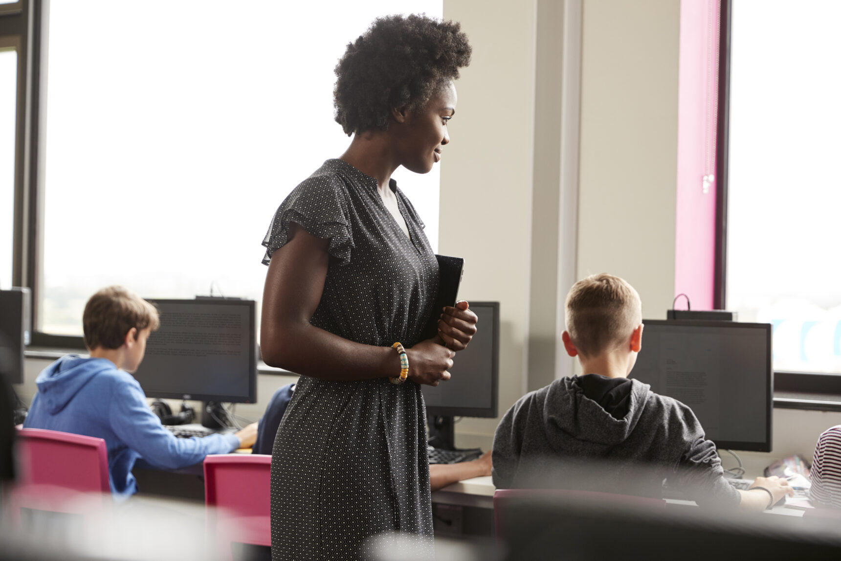 Female supply teacher supervising students at computers.