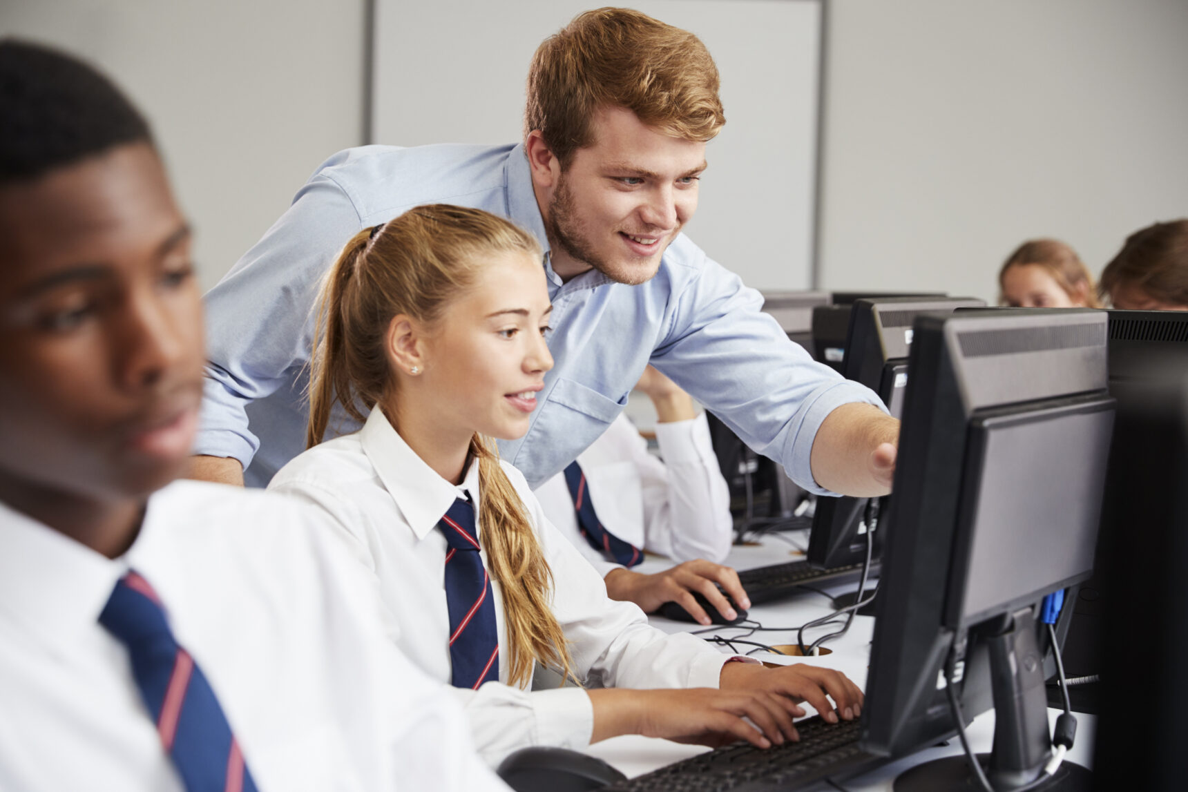 Supply teaching helping female pupil at computer.