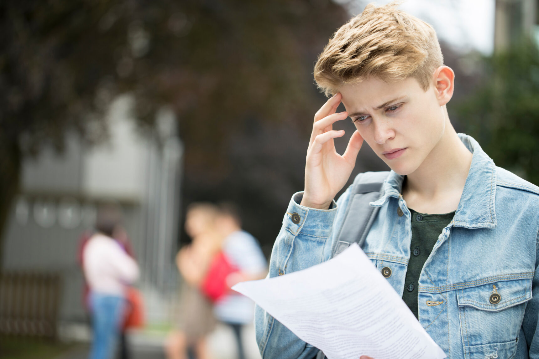 A teenage boy stands holding a university offer letter, looking confused and disappointed.