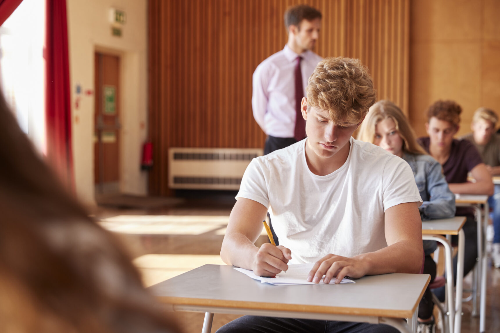 A student focused on answering questions during an exam in an exam hall.