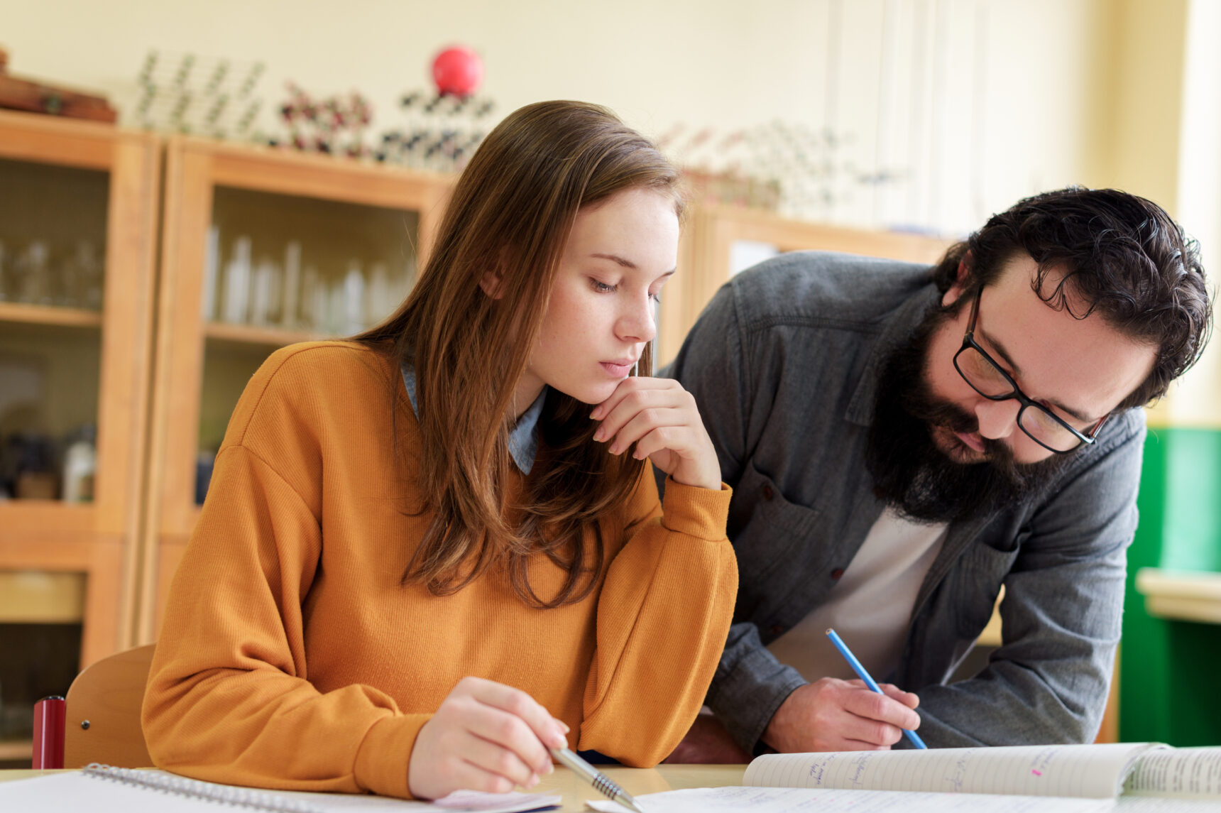 A tutor supports a student with practising exam questions at a classroom desk.